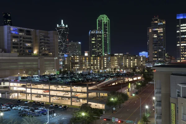 Lights of the Dallas skyline beyond a lit up parking garage — Stock Photo, Image