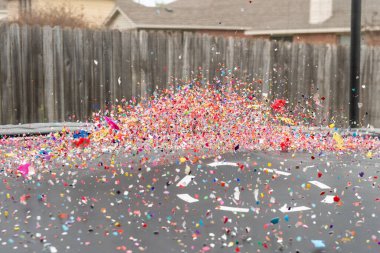 Renkli bir konfeti ve yumurta kabuğu yığını arka bahçedeki bir trambolinin yüzeyinden sekerken havada uçuşuyor..