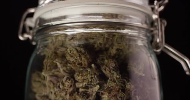 Burk med torkade och behandlade cannabisknoppar. Medicinsk marijuana roterar på en svart bakgrund närbild. — Stockvideo