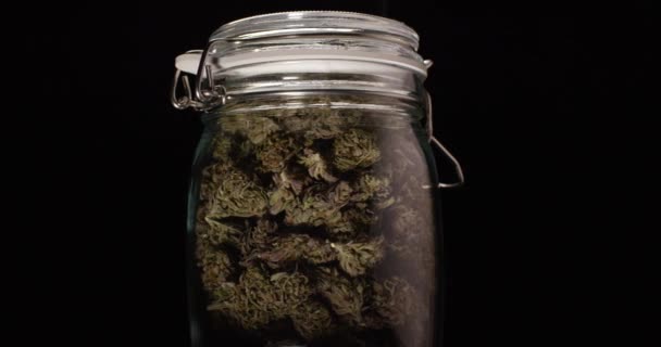 乾燥した大麻の芽のジャー。黒い背景で回転する医療用マリファナが近くに. — ストック動画