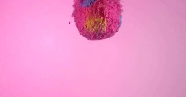 Pink colorful bath bomb falling down into clean water in slow motion against light pink background. — Stock Video