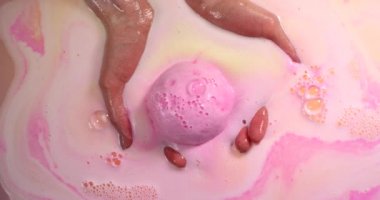 Sıcak suda pembe renkli bir banyo bombasını tutan kadın elleri.