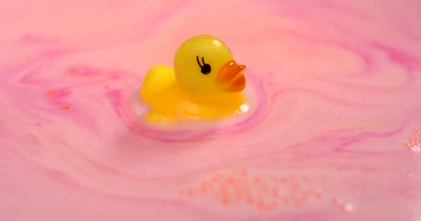 Bonito brinquedo de pato amarelo flutua em um close-up de espuma colorido rosa. — Vídeo de Stock