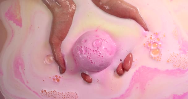 Kvinnliga händer håller en rosa färgglad bad bomb i ett varmt vatten. — Stockvideo