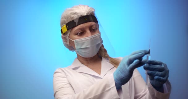 Female doctor wearing protective face shield and white uniform holding a syringe and preparing for covid 19 or other vaccine injection. — Stock Video