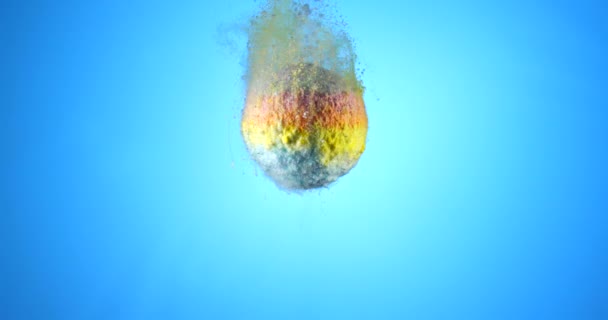 Colorida bomba de baño cayendo en agua limpia sobre fondo azul. Filmado en cámara lenta con cámara RED — Vídeo de stock
