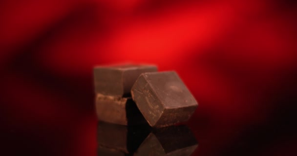 Donkere chocolade blokjes draaien op rode achtergrond. Close-up weergave gefilmd met RED camera. — Stockvideo