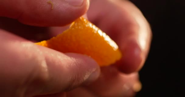 Männliche Hände drücken Orangenhaut auf schwarzen Hintergrund. Orangefarbenes Fruchtspray sprudelt aus nächster Nähe. Aufgenommen in Zeitlupe mit ROTER Kamera. — Stockvideo