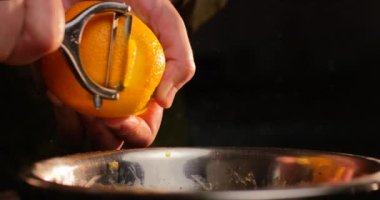 Erkek eller, siyah arka planda özel bir aletle portakal meyvesi soyuyorlar. Kırmızı kamerayla yavaş çekimde yakın çekim yap.