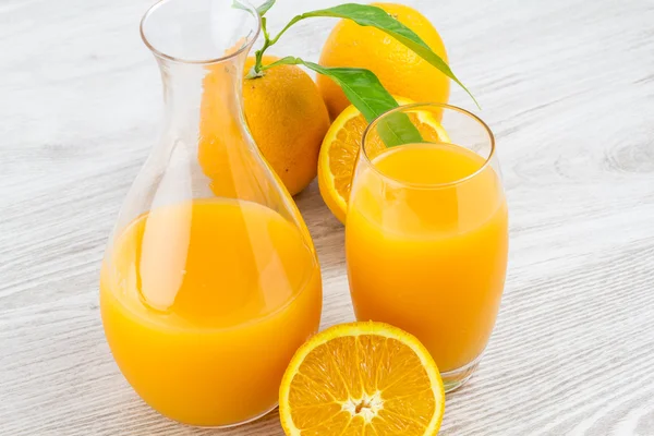 Апельсини і склянка соку на дерев'яному столі — стокове фото