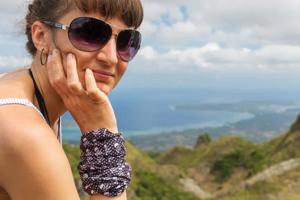 young thinking woman with sunglasses is sitting one mountains and looking at the camera