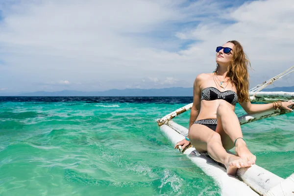 Unga europeiska kvinna med solglasögon sitter på båten i tropiska turkosa havet och att få tan på solig dag — Stockfoto