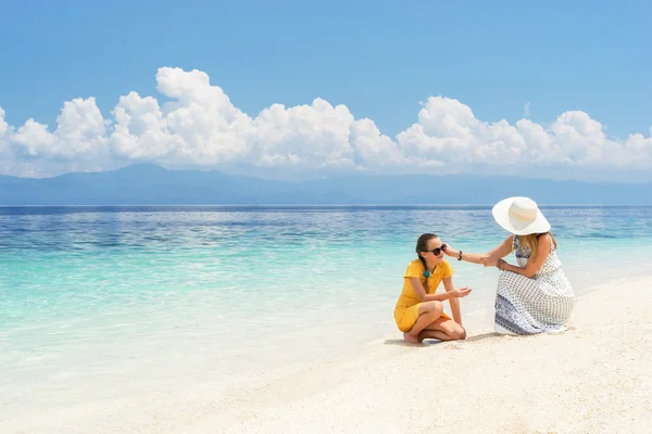 Youn Europese vrouw in lichte jurk zit op het witte zand strand in de buurt van prachtige tropische zee en zorgen over haar tiener dochter op zonnige dag — Stockfoto