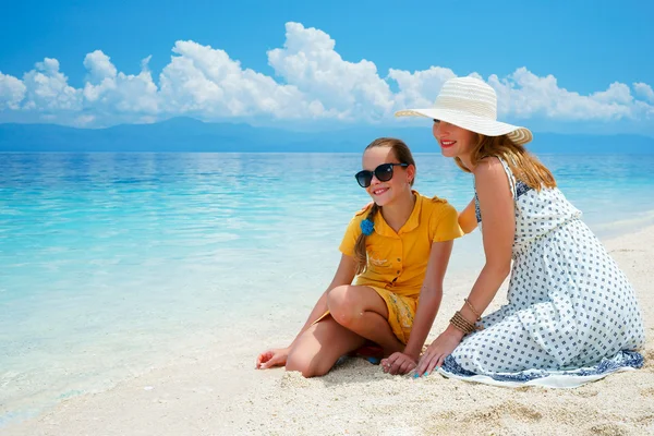 Youn Europese vrouw in lichte jurk zit op het witte zand strand in de buurt van prachtige tropische zee en zorgen over haar tiener dochter op zonnige dag — Stockfoto