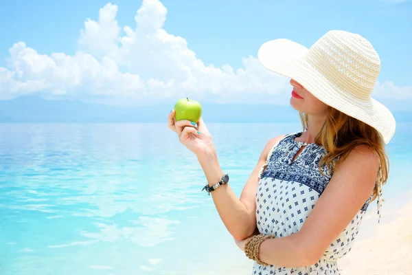 Jonge mooie Europese vrouw houdt groene appel in haar hand tegen de kalme zachte tropische zee onder inschrijving blauwe hemel — Stockfoto