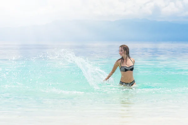 Jonge Europese vrouw in bikini met goed humeur spatten en dansen in mooie tropische kalme zee onder een bewolkte hemel van de zachte — Stockfoto