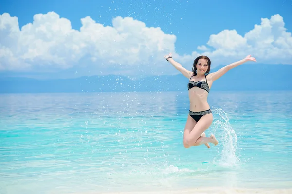Jonge Europese vrouw is Jumping op het strand van tropische kalme zee met witte zand en blauwe hemel — Stockfoto