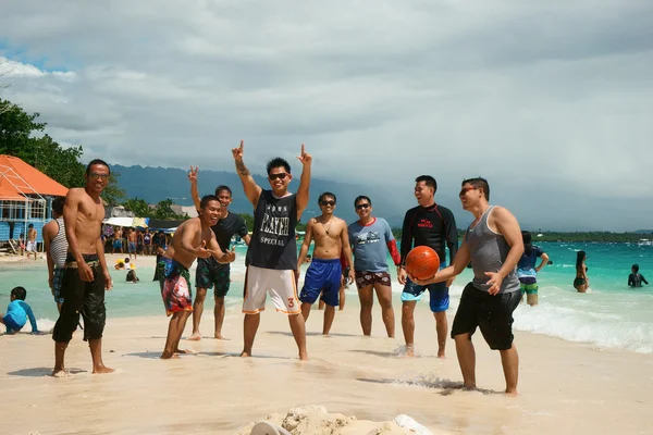 Moalboal. Cebu. Filipinler - 06 Ağustos 2016: Filipin arkadaş basketboll ile büyük şirket yakın turkuaz dalgalı deniz fırtınalı gökyüzü altında tropik sahilde eğlenceli oluyor