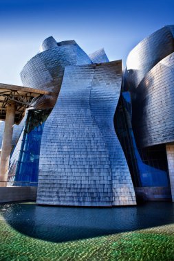Stunning architectural photography of the Guggenheim Museum Bilbao, captured at dusk. The iconic titanium-clad curves of Frank Gehry's masterpiece reflect the warm, golden light of sunset and the calm waters of the Nervin River.