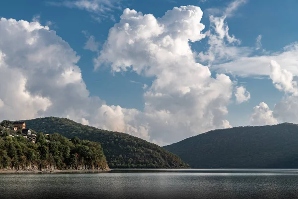 Evening clouds are reflected in the calm waters of lake Abrau, surrounded by green hills.