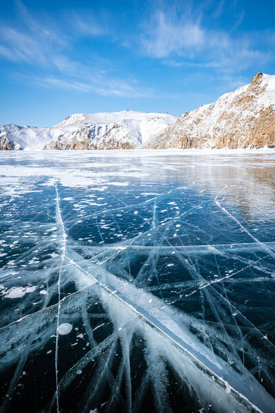 Длинные, извилистые трещины простираются за горизонт по темному, бесконечному льду озера Байкал