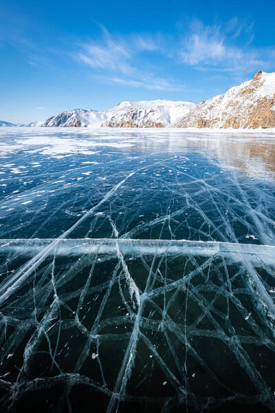 Длинные, извилистые трещины простираются за горизонт по темному, бесконечному льду озера Байкал