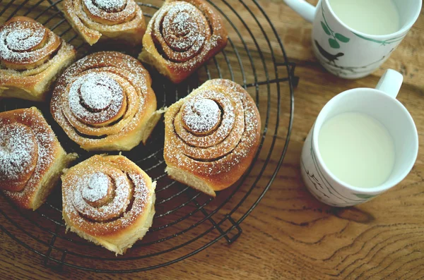 Homemade cinnamon buns with a cup of milk on a cooling rack