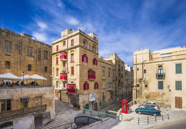 Мальта, Валлетта - Древние мальтийские дома с традиционными красными балконами и окнами и красной телефонной будкой
