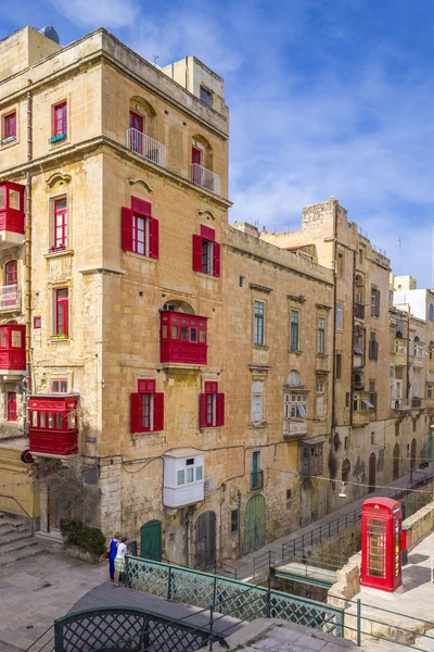 Malta, Valletta - Vista para a rua com turistas, cabine telefónica vermelha e tradicionais varandas vermelhas, janelas — Fotografia de Stock