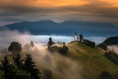 Jamnik, Slovenya - Jamnik St. Primoz Tepe Kilisesi 'nde büyülü sisli bir yaz sabahı. Gün doğumunda. Sis nazikçe altın gökyüzü ve arka planda Julian Alps olan küçük şapelin arkasına gider.
