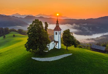 Skofja Loka, Slovenya - Sveti Tomaz 'ın (Saint Thomas) güzel tepe kilisesinin havadan görünüşü ve yaz mevsiminde inanılmaz sisli gündoğumu ve Julian Alpleri