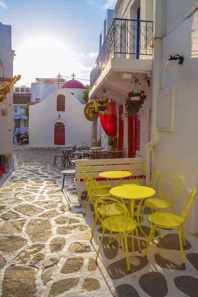 Mykonos streetview napfelkeltekor a kápolna és a sárga székek és asztalok, Görögország — Stock Fotó