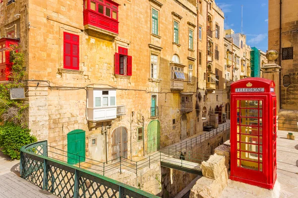 Streetview Valletta s tradiční červené balkony, staré červené telefonní budky a modrá obloha - Malta — Stock fotografie