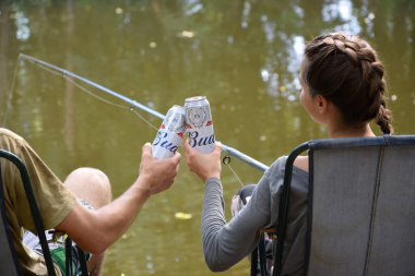 KHARKOV, UKRAINE - 22 Ağustos 2020: Erkek ve kız balıkçılık sırasında Budweiser Alkollü Bira Kutusu ile tezahürat yapıyor. Budweiser, Anheuser-Busch Inbev 'den Amerika' nın en popüler markasıdır.