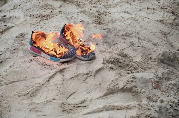 近くの砂浜の海岸に立つ火の上でスポーツスニーカーやジムの靴を燃焼 選手は燃え尽きた トレーニングコンセプト中の身体的運動 — ストック写真