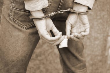 Tutuklanmış, elleri kelepçeli, arka planında eroin paketi olan bir uyuşturucu satıcısı. Yasadışı uyuşturucu kaçakçılığı kavramı