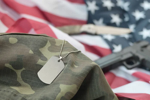 Army Dog tag token with 9mm bullets and pistol lie on folded United States flag and camouflage uniform. A set of US military veteran items or old duty trophy kit