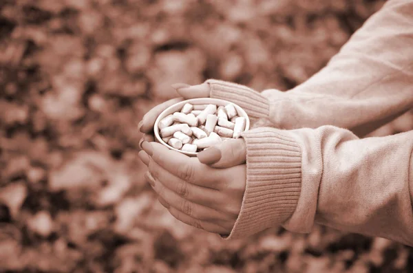 Woman wearing white sweater in their hands holding a big coffee cup in a relaxed mood on foliage background