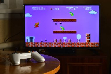 KHARKOV, UKRAINE - NOVEMBER 12, 2020: Dendy video oyun denetleyici masada Super Mario Bros oyunu büyük ekranda