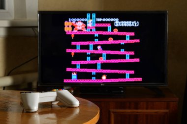 KHARKOV, UKRAINE - NOVEMBER 12, 2020: Dendy video oyun denetleyici masada Donkey Kong oyunu büyük ekranda