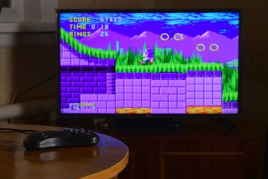 KHARKOV, UKRAINE - NOVEMBER 12, 2020: Sega mega sürüş video oyun denetleyici ve Kirpi Sonic oyunu büyük ekranda