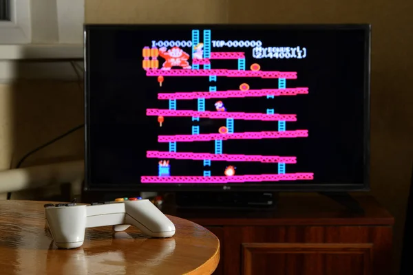 KHARKOV, UKRAINE - NOVEMBER 12, 2020: Dendy video oyun denetleyici masada Donkey Kong oyunu büyük ekranda