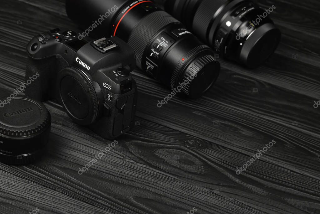 KHARKOV, UKRAINE - NOVEMBER 23, 2020: Canon EOS R photocamera and mount adapter EF - EOS R with Canon 105mm f2.8 and Sigma 24-105 f4 Art lenses on black wooden table
