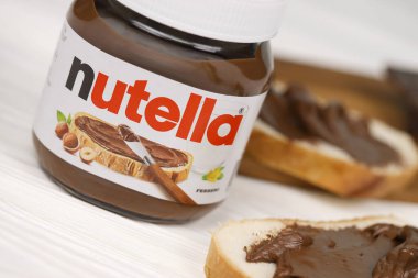 KHARKOV, UKRAINE - 27 Aralık 2020: Nutella cam kutu ve taze pişmiş ekmek üzerine yayılmış. Nutella, İtalyan Ferrero firması tarafından 1964 yılında üretilmiştir.