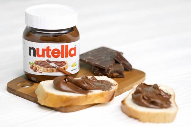 KHARKOV, UKRAINE - 27 Aralık 2020: Nutella cam kutu ve taze pişmiş ekmek üzerine yayılmış. Nutella, İtalyan Ferrero firması tarafından 1964 yılında üretilmiştir.