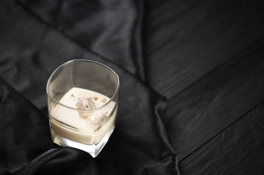 Koyu kumaş ve ahşap bar arka planında buz küpleri olan bir bardak İrlanda kremalı baileys likörü. Ev yapımı lüks elit alkol kokteyli. Metnin için yer