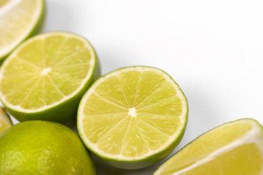 Açık beyaz masada bir sürü sarı limon ve yeşil limon dilimleri var. Mutfakta taze meyve var.