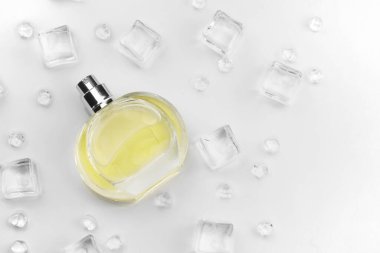 Kadın parfümü sarı şişe, buz küplerinde parfüm şişesinin objektif fotoğrafı ve beyaz masanın üzerindeki su. Yukarıdan bak. Model ürün fotoğrafı, tazelik ve aroma konsepti