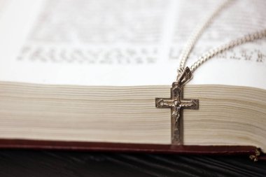 Üzerinde haç olan gümüş kolye siyah ahşap masadaki kutsal Hristiyan kitabının üzerinde. Kutsallığın gücüyle Tanrı 'dan dua etmek, şans getirir ve affedicidir..