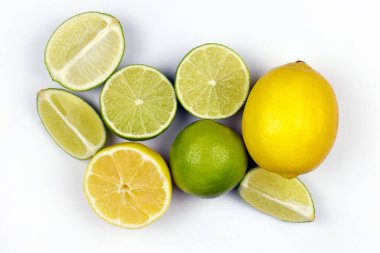 Açık beyaz masada bir sürü sarı limon ve yeşil limon dilimleri var. Mutfakta taze meyve var.